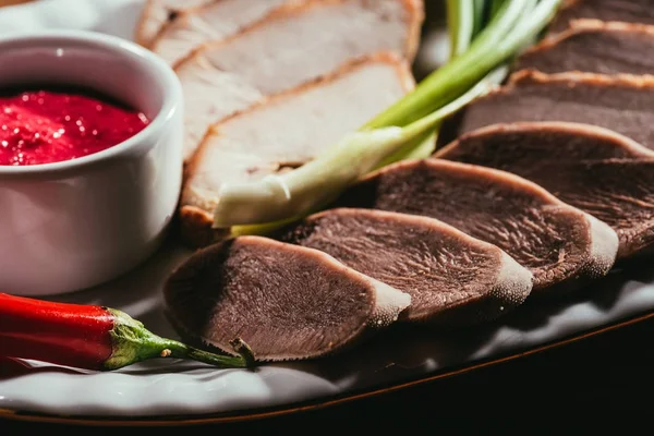 Vista de perto de fatias de carne variadas servidas com molho, cebola verde e pimenta no prato branco — Fotografia de Stock