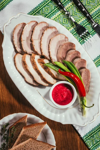 Вид ветчины, нарезанной на белой тарелке с блюдцем и красным перцем поверх полотенца на столе — стоковое фото