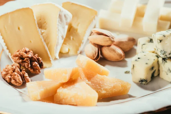 Unpeeled pistachios and peeled walnuts laying on plate with cheese slices — Stock Photo