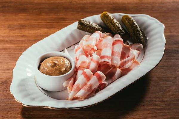 View of cold-boiled pork with mustard in saucer on white plate over wooden surface — Stock Photo