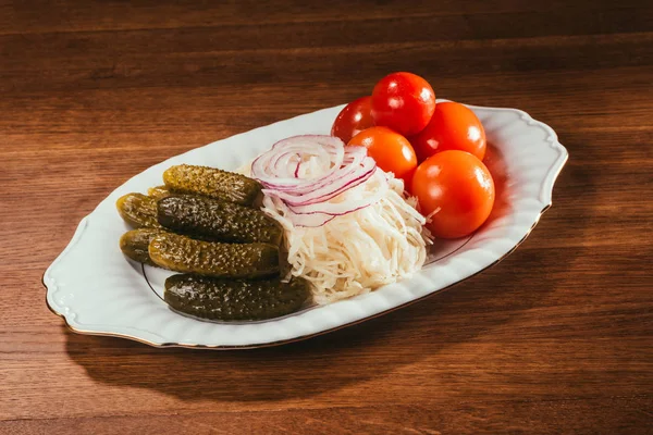 Cetrioli di sale marinati, cavolo acidulo con anelli di cipolla e pomodoro crudo adagiato sul piatto su una superficie di legno — Foto stock