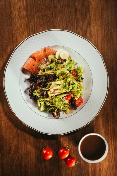 Hojas de ensalada mezcladas con verduras puestas en el plato con algunas rebanadas de pescado - foto de stock