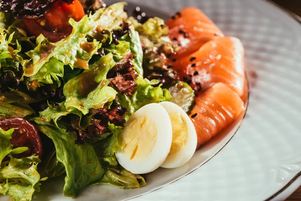 Hojas de ensalada mezcladas con verduras puestas en el plato con algunas rebanadas de pescado - foto de stock