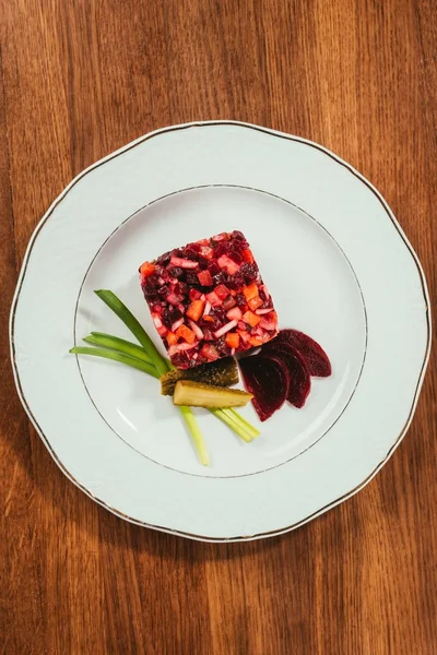 Vue du dessus de la salade Vinegret servie avec oignon vert et concombre mariné sur assiette blanche sur table en bois — Photo de stock