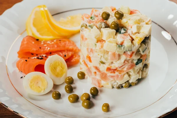 Russian salad on plate with scattered peas, boiled eggs and fish slices — Stock Photo