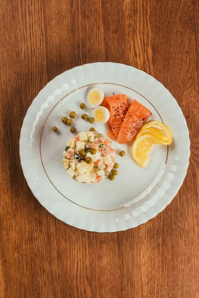 Russian salad on plate with scattered peas, boiled eggs and fish slices — Stock Photo