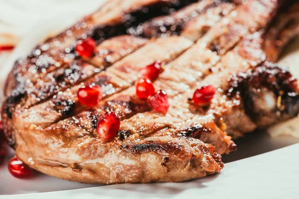 Vista ravvicinata della carne alla griglia con semi di melograno su piatto bianco — Foto stock