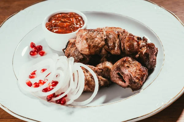 Pork slices laying on plate with sauce and sliced onion rings with pomegranate seeds — Stock Photo