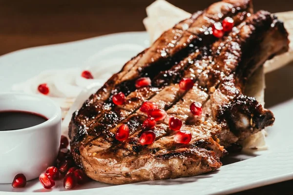 Vista de cerca de la carne a la parrilla con semillas de cebolla y granada en un plato blanco - foto de stock