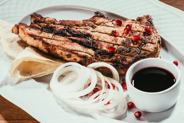 Vista de cerca de la carne a la parrilla con semillas de cebolla y granada en un plato blanco - foto de stock