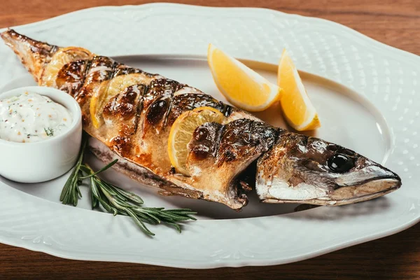 Pesce fritto steso su piatto bianco con fette di arancia e salsa su superficie di legno — Foto stock