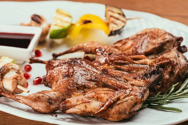 Grilled chicken laying on white plate with saucer on blurred background — Stock Photo