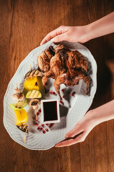 Обрезанное изображение рук, держащих поддон с жареной птицей и овощами — стоковое фото