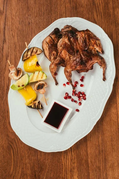 Pollo a la parrilla que pone en el plato con verduras fritas en el pincho cerca del platillo sobre la superficie de madera - foto de stock