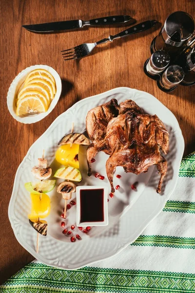 Верхний вид на жареные овощи на тарелке с жареной курицей на деревянном столе с салфеткой — стоковое фото