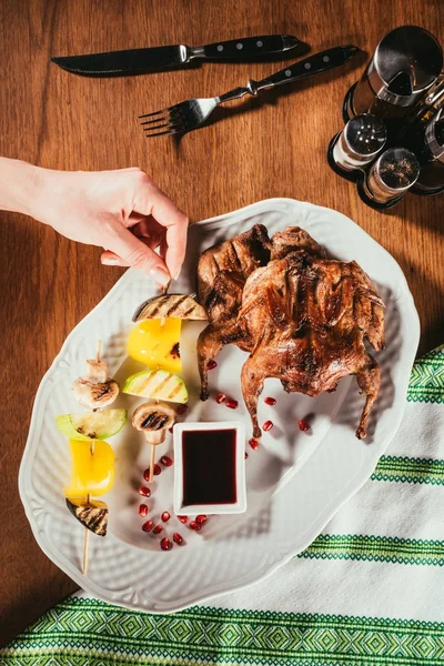 Vista superior de la mano femenina tomando trozo de verduras a la parrilla de plato con pollo frito - foto de stock