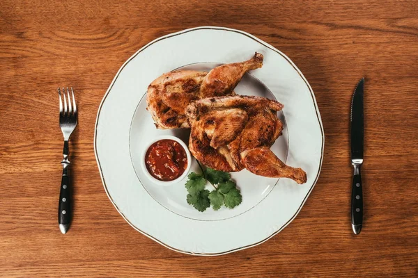 Blick von oben auf gegrilltes Hühnchen auf Teller mit Sauce auf Holztisch — Stockfoto