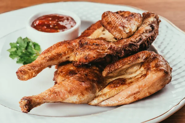 Grilled chicken laying on white plate with saucer on background — Stock Photo