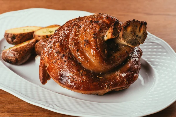 Fried meat with bone inside laying on plate with potatoes over wooden surface — Stock Photo