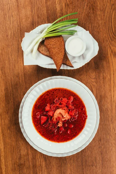 Vista superior del plato de borscht en plato blanco servido con pan de centeno en mesa de madera - foto de stock