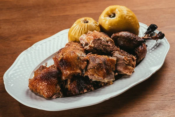 Pezzi d'anatra fritti che posano su piatto con mele marinate sopra tavolo di legno — Foto stock