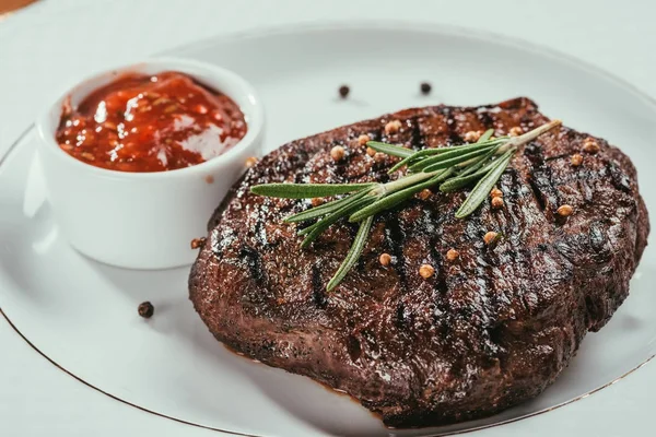 Vista de perto do bife grelhado com pimenta, alecrim e molho no prato branco — Fotografia de Stock