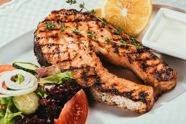 Close-up view of grilled salmon fish pieces with lemon, herbs and salad on white plate — Stock Photo