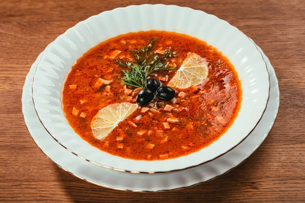 Soljanka-Suppe mit Oliven und Zitrone auf weißem Teller über Holzoberfläche — Stockfoto