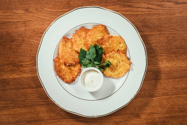 Vista superior de panqueques de patata servidos con salsa de crema agria en el plato en la mesa de madera - foto de stock