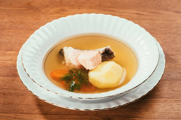 Soupe chaude au saumon et légumes servie dans une assiette blanche sur une table en bois — Photo de stock