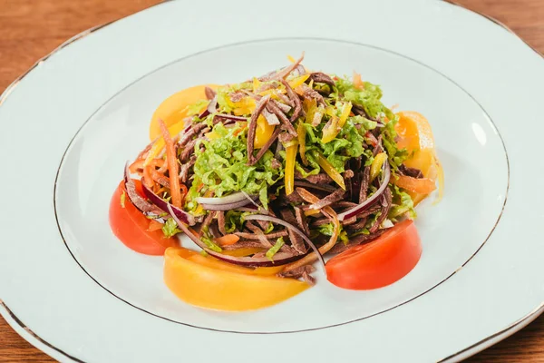 Frisches Gemüse in Scheiben geschnitten auf weißem Teller über hölzerne Oberfläche — Stockfoto