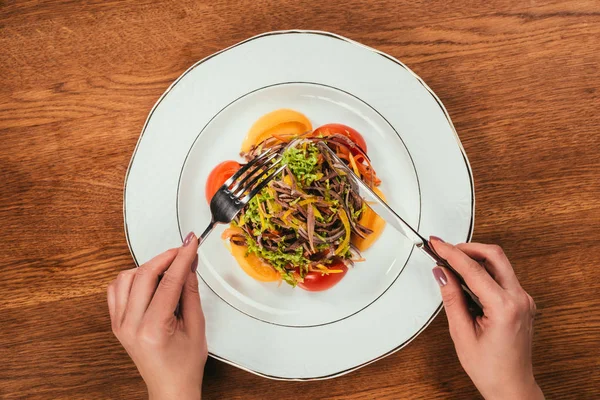 Top view of woman eating fresh vegetable salad served on white plate on wooden table — Stock Photo