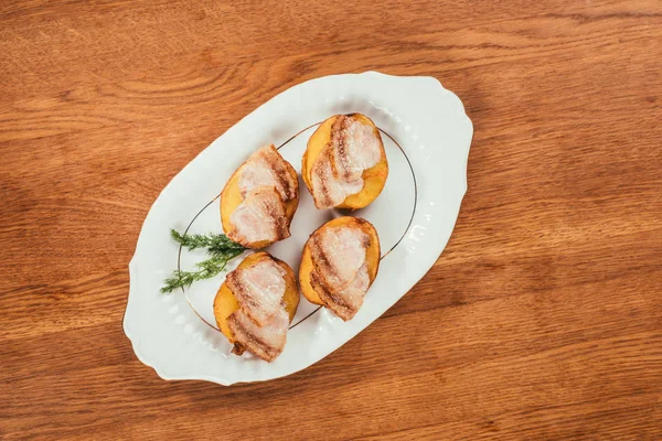 Patatas al horno con rodajas de jamón en la parte superior de la colocación en el plato sobre la superficie de madera - foto de stock