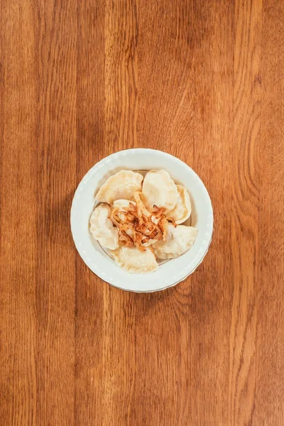 Gnocchi con cipolle fritte in cima che posano in piatto sopra superficie di legno — Foto stock