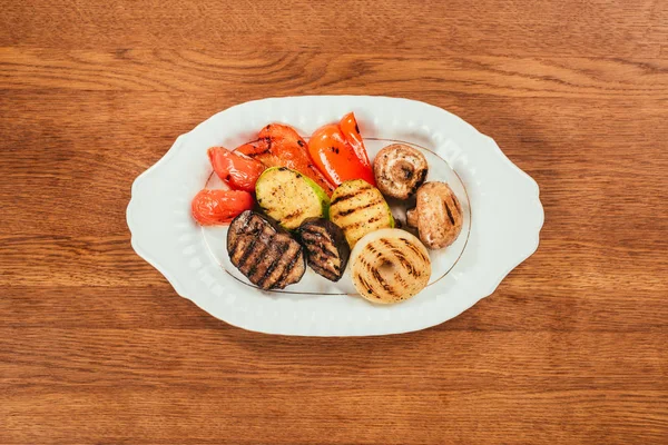 Вид сверху на грибы и овощи на белой тарелке на деревянном столе — стоковое фото