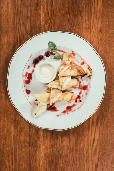 Vista superior de panquecas de crepe doce com geléia e creme de leite na placa na mesa de madeira — Fotografia de Stock