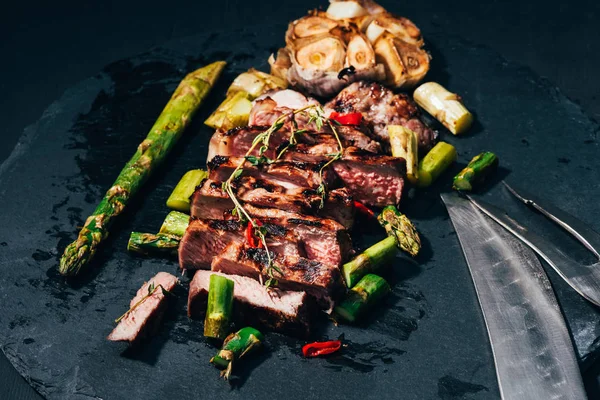 Vue rapprochée de délicieuses tranches de viande grillée juteuse avec des épices et des asperges sur noir — Photo de stock