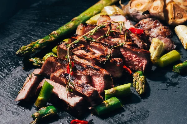 Vista de perto da carne grelhada em fatias gourmet com espargos e especiarias em preto — Fotografia de Stock