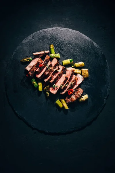 Vista superior de saborosa carne grelhada fatiada com espargos em placa de ardósia preta — Fotografia de Stock