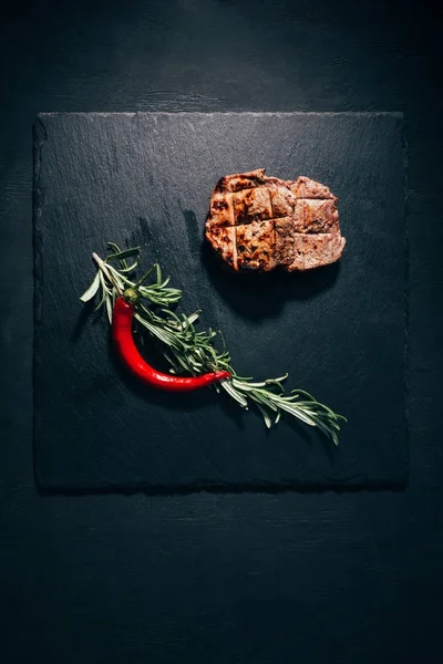 Vista superior de bife grelhado gourmet com alecrim e pimenta no quadro de ardósia preta — Fotografia de Stock