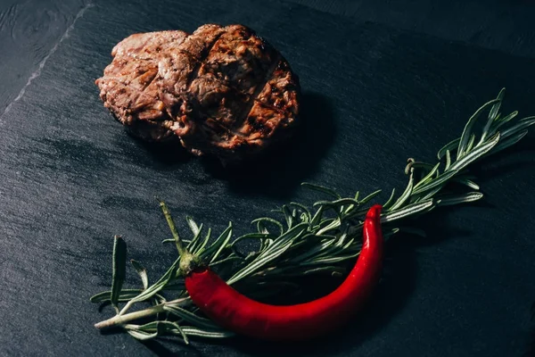 Close-up view of delicious grilled steak with rosemary and chili pepper on black — Stock Photo