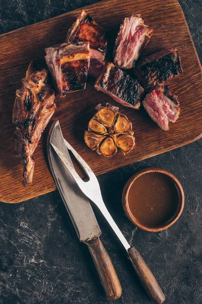 Vista superior de deliciosa carne grelhada com garfo, faca e molho em preto — Fotografia de Stock