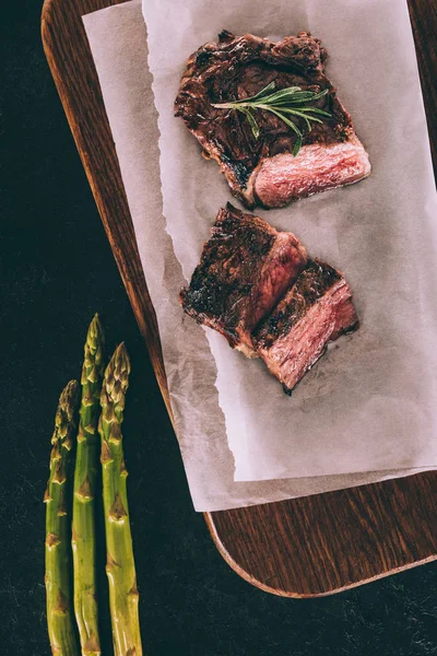 Vista superior de deliciosa carne grelhada em papel manteiga e espargos em preto — Fotografia de Stock