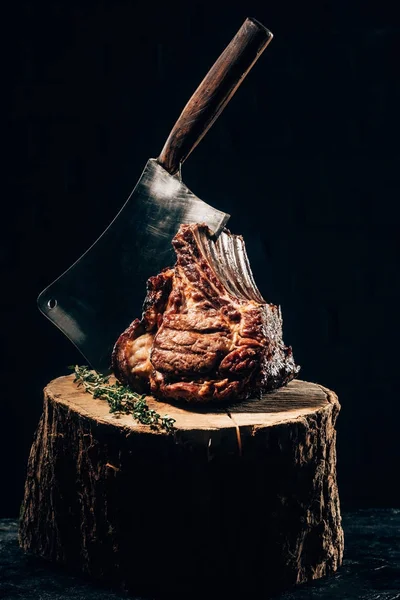 Close-up view of delicious grilled ribs with meat knife and rosemary on wooden stump — Stock Photo