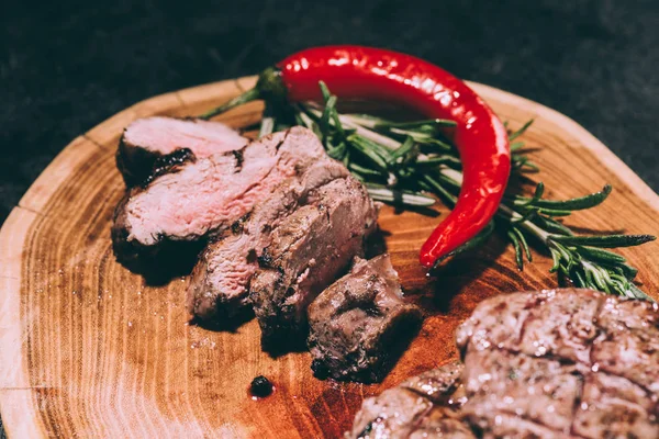 Vista de cerca de la carne a la parrilla en rodajas con romero y chile sobre tabla de madera - foto de stock