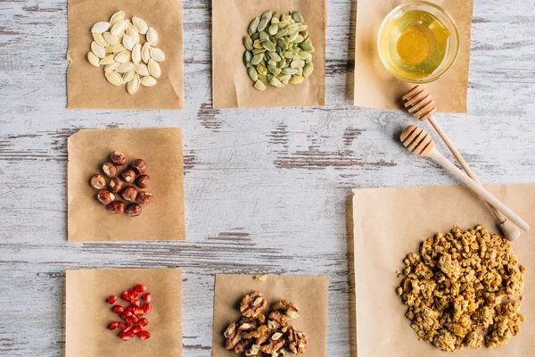 Top view of granola ingredients on baking parchment pieces and honey sticks on table — Stock Photo