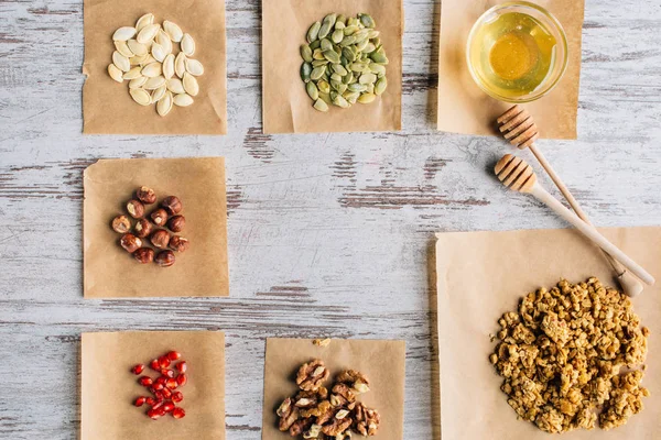 Vista superior de los ingredientes de granola en piezas de pergamino para hornear y palitos de miel en la mesa - foto de stock