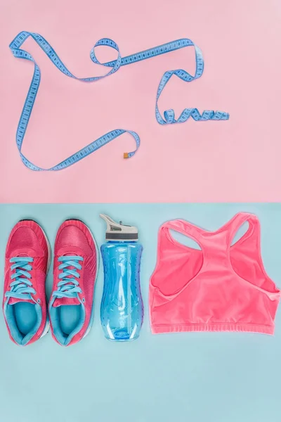 Sports equipment with shoes, measuring tape and sports top isolated on pink and blue — Stock Photo