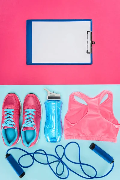 Équipement de sport avec chaussures, corde à sauter, haut de sport et presse-papiers isolés sur rose et bleu — Photo de stock