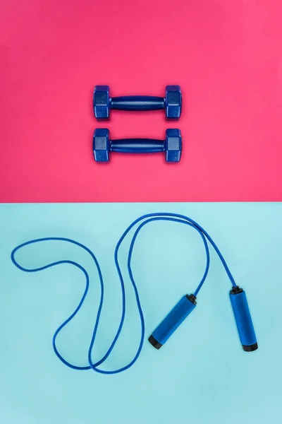 Dumbbells esportivos e pulando corda isolada em rosa e azul — Fotografia de Stock